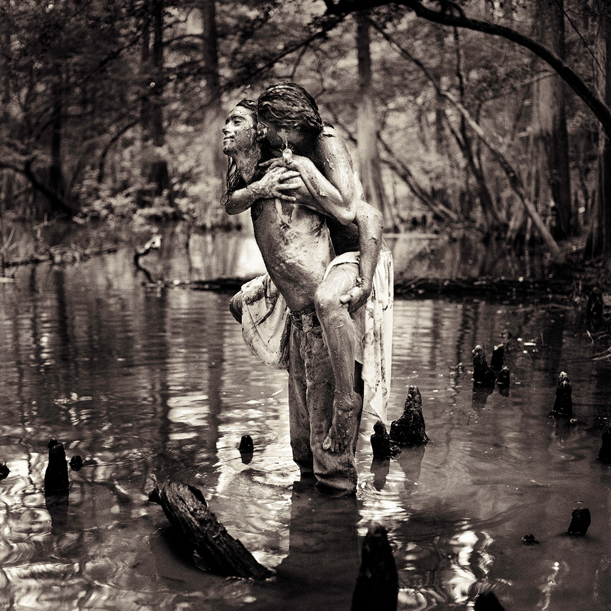 Woman clings to the back of a man as they stand in the swamp