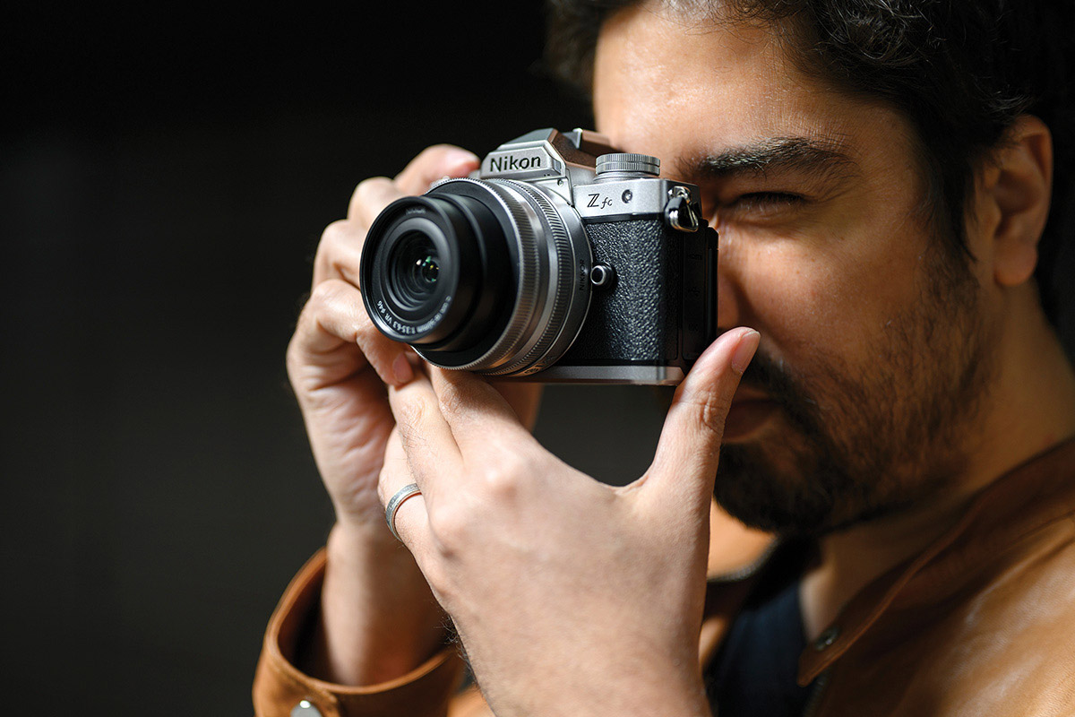 A person with beard and mustache holding the Nikon Z fc camera viewfinder up to his eye.
