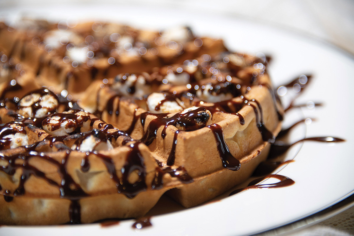 Close up of a waffle with chocolate drizzle on a white plate