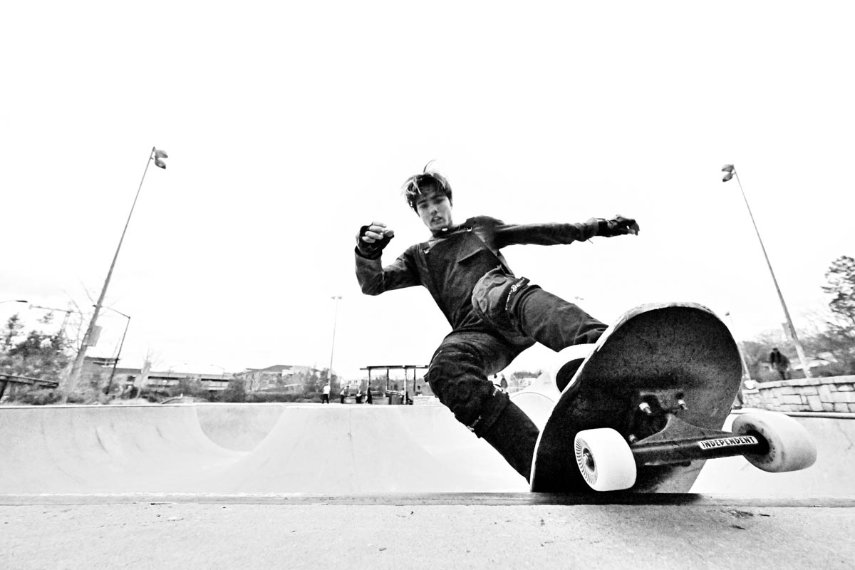 Actions shot, black-and-white, young person on a skateboard caught at the moment the board is at the lip of a wall at a skate park