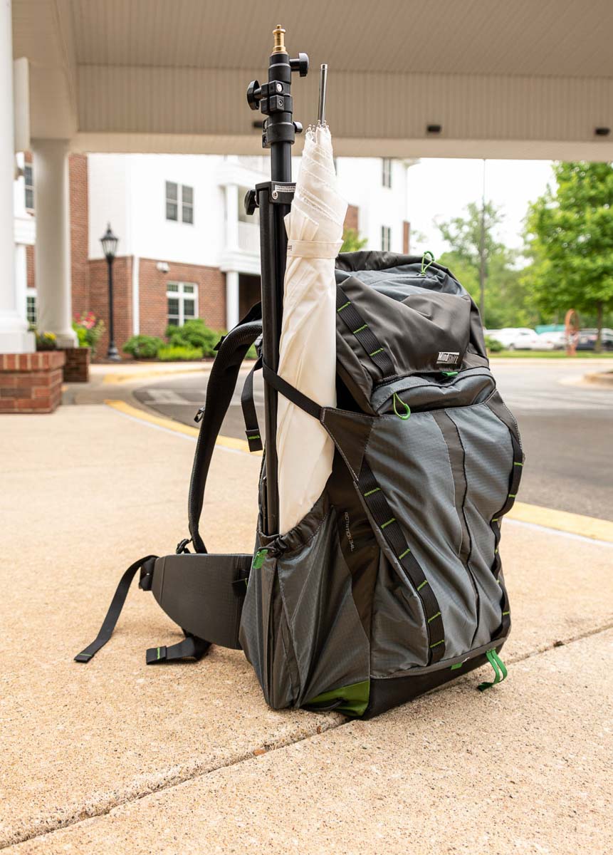 MindShift Rotation backpack sitting upright on a sidewalk with a light stand and white umbrella in the tripod sleeve