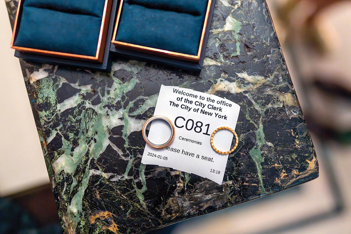 Two wedding rings are placed on top of the torn ticket number for office of the City Clerk of the State of New York. They are on top of a green and black marble ledge.