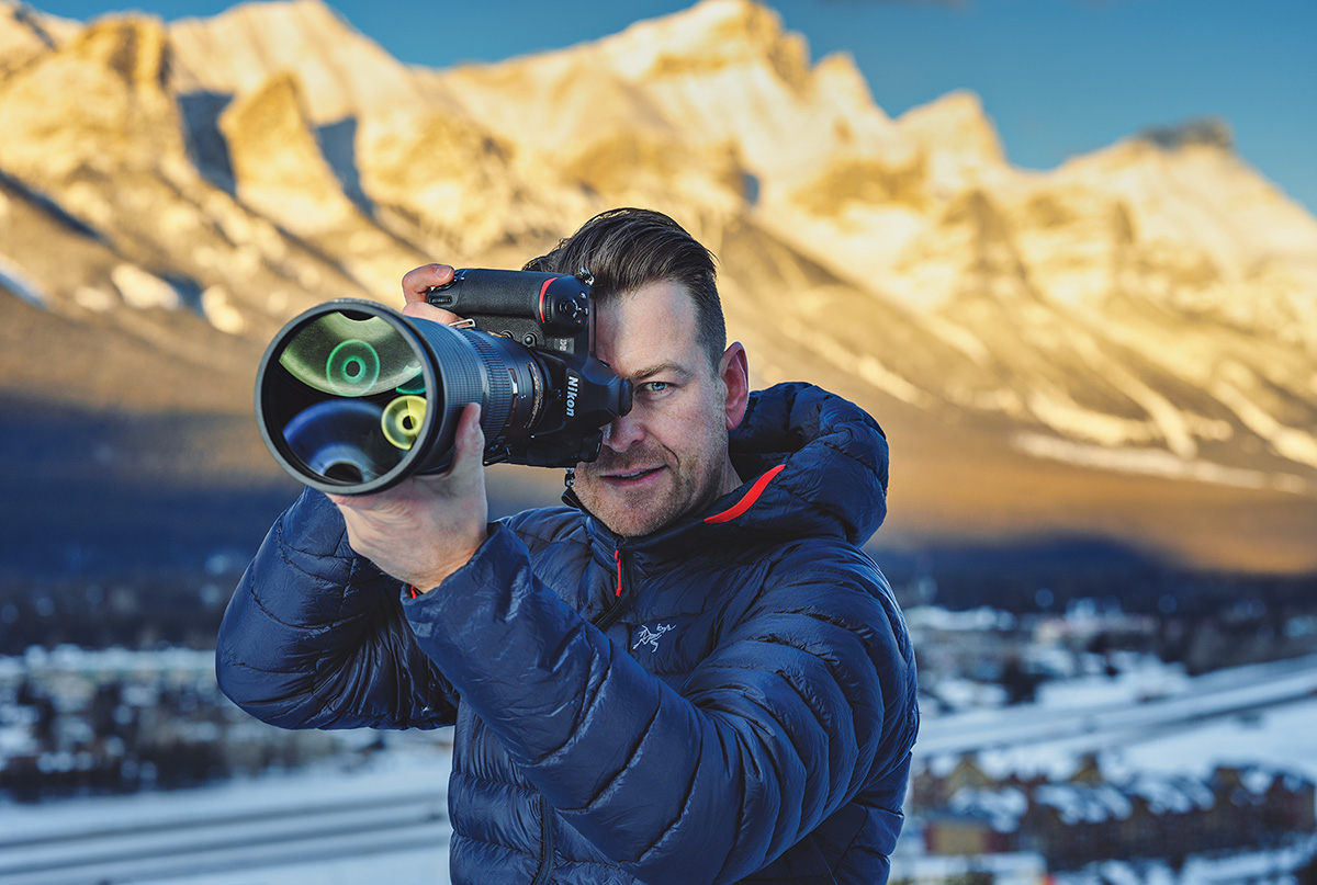 Portrait of photographer Kristian Bogner holding a camera, with mountains in the background