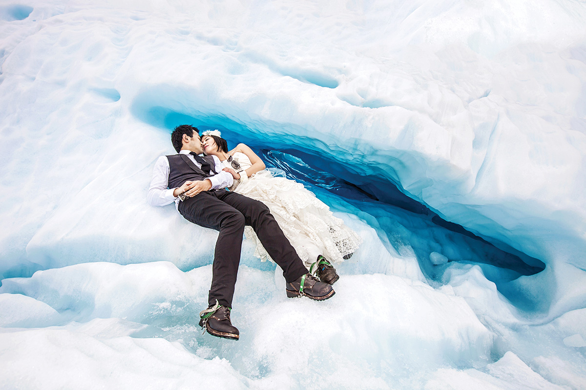 Bride and groom lying on icy glacier